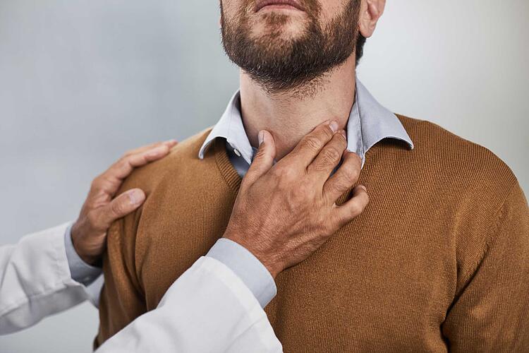 Die Hand eines Arztes tastet den Hals eines Mannes ab.