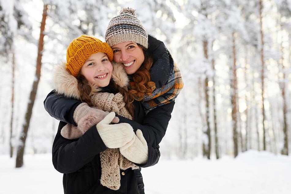 Mutter und Tochter umarmen sich bei einem Spaziergang im Schnee