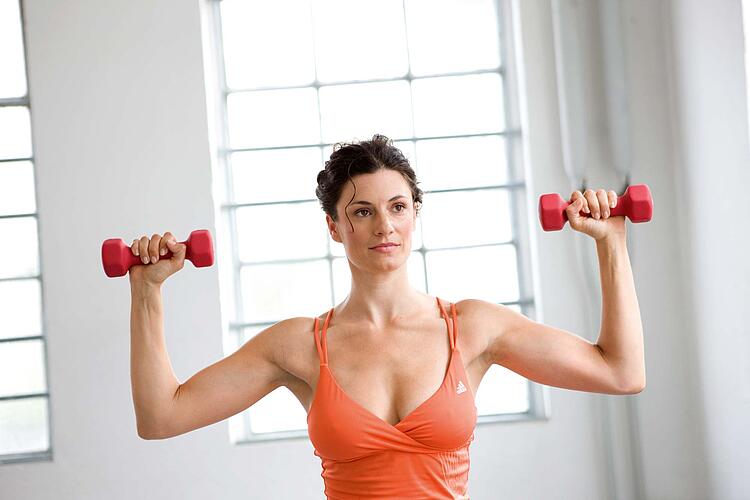 Junge Frau in Sporttop trainiert mit Kurzhanteln in einem Fitnessstudio.