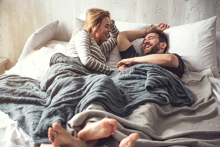 Paar liegt im Bett und unterhält sich lachend.