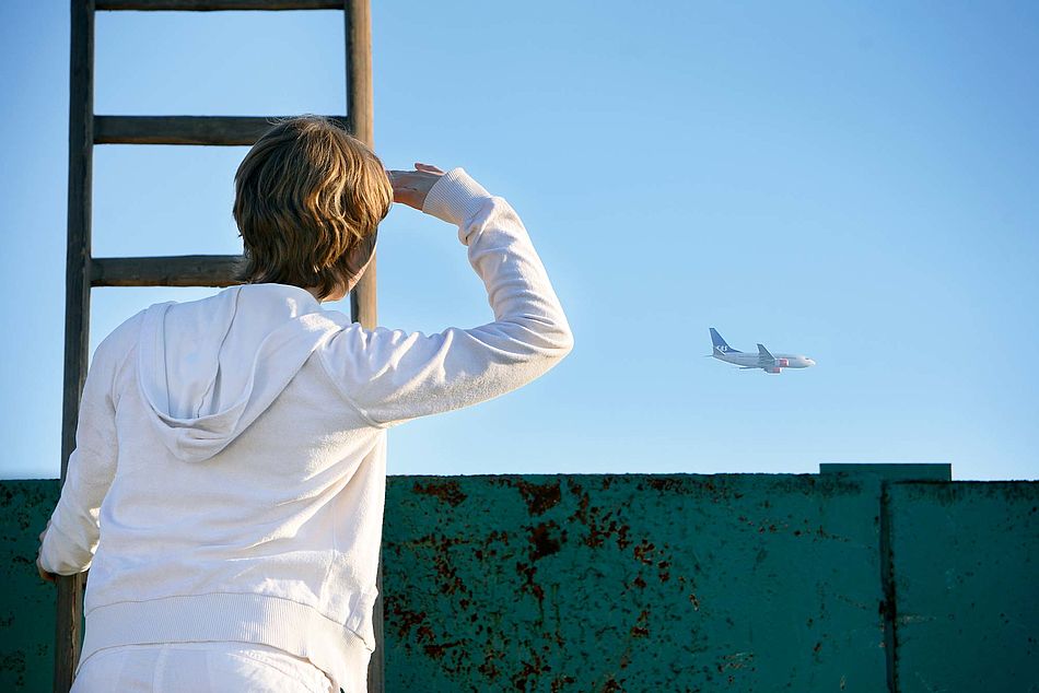 Eine Frau steht auf einer Leiter und beobachtet ein Flugzeug am Horizont. - Bildnachweis: © wdv / Oana Szekely Eine Frau steht auf einer Leiter und beobachtet ein Flugzeug am Horizont.