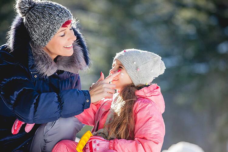 Mutter cremt Tochter das Gesicht ein, um es vor Kälte zu schützen