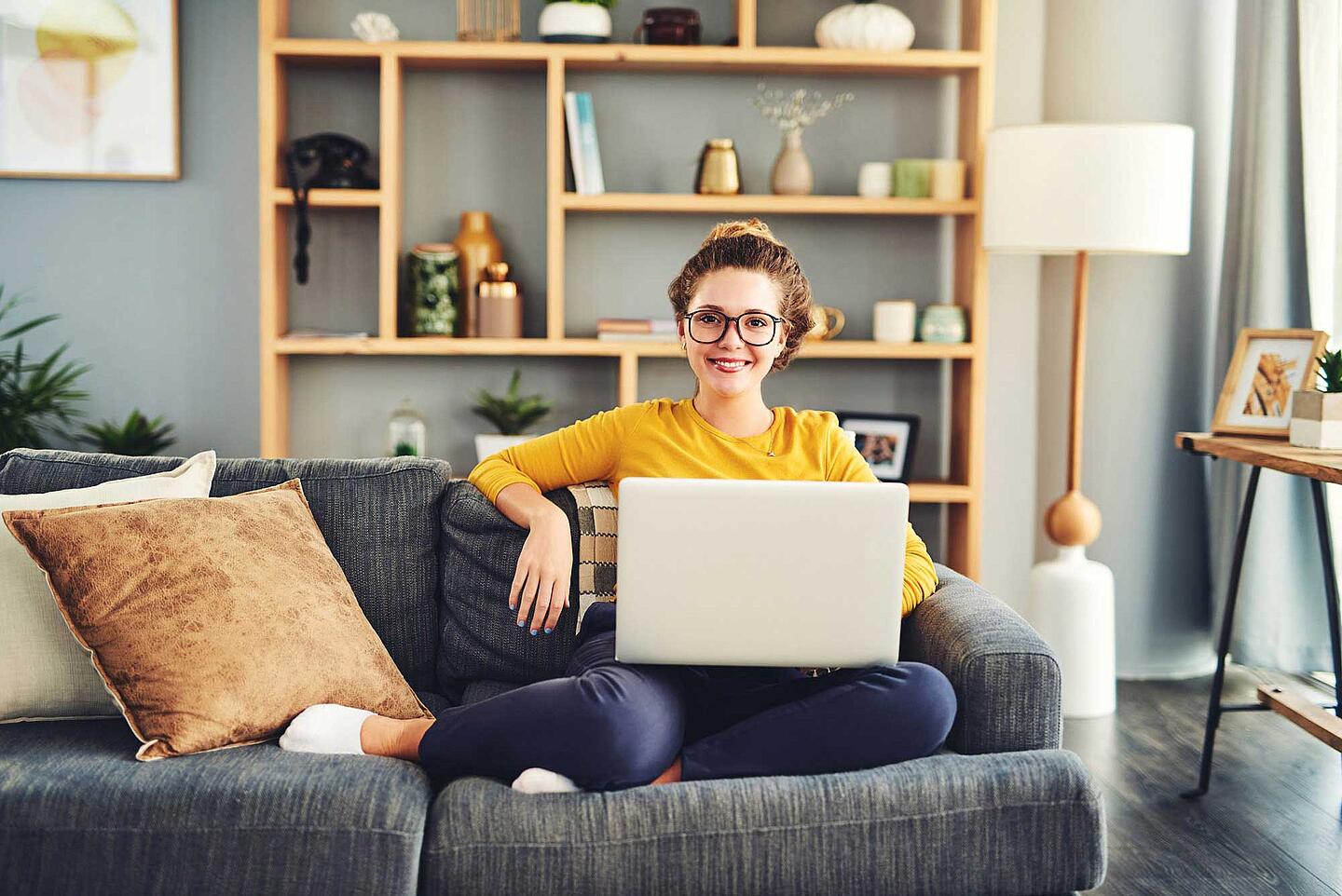 Frau sitzt mit dem Laptop auf dem Sofa.