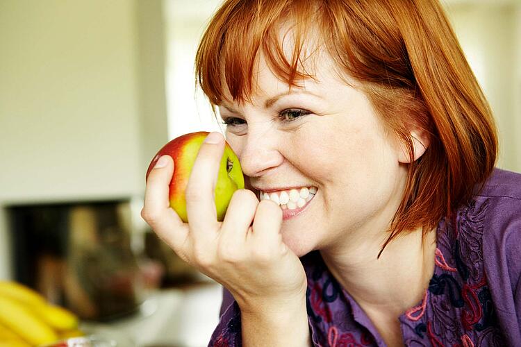 Junge Frau hält einen Apfel in der Hand.