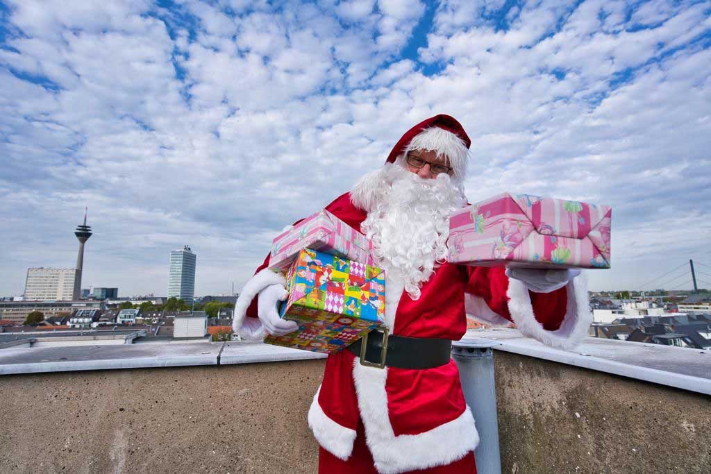 Weihnachtsmann Andreas Vogt mit Geschenken im Arm auf dem Dach eines Hochhauses